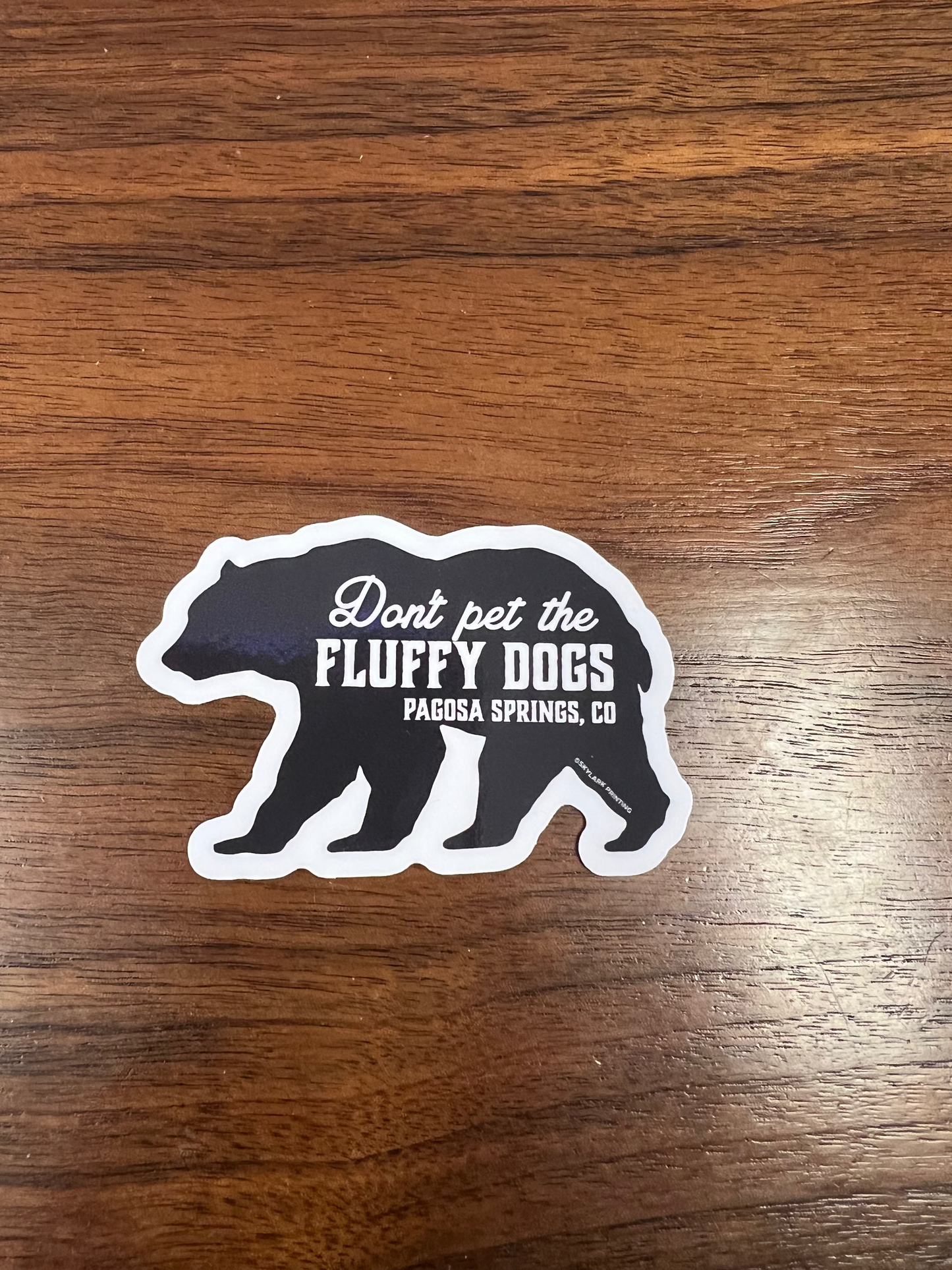 Sticker with text 'Don't pet the fluffy dogs' on a wooden surface