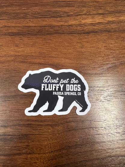 Sticker with text 'Don't pet the fluffy dogs' on a wooden surface